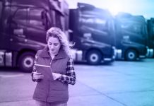 Truck driver holding tablet and checking route for new destination. In background parked truck vehicles. Transportation service.